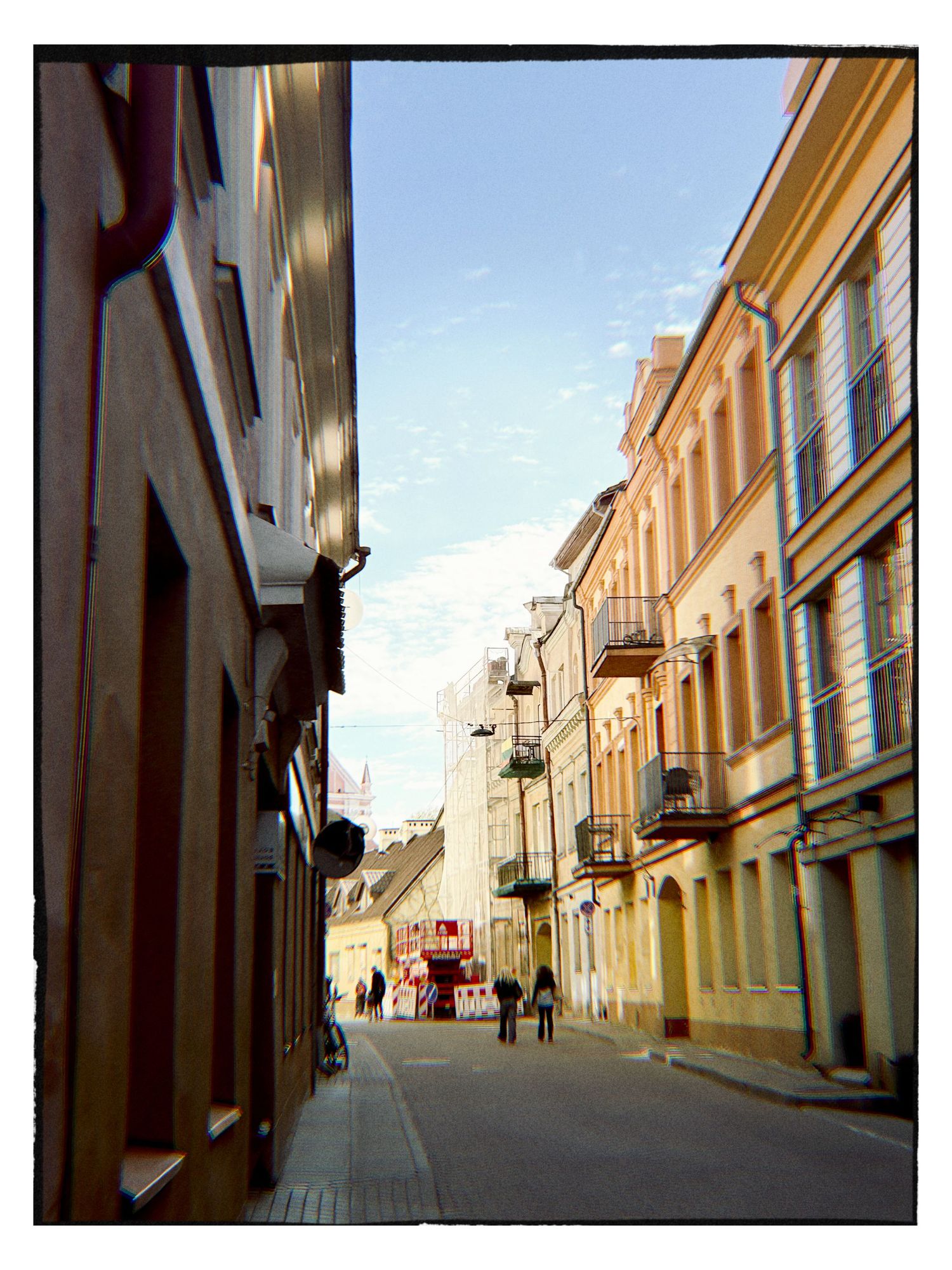 Narrow cobblestone street lined with colorful historic buildings under a blue sky in a European old town.