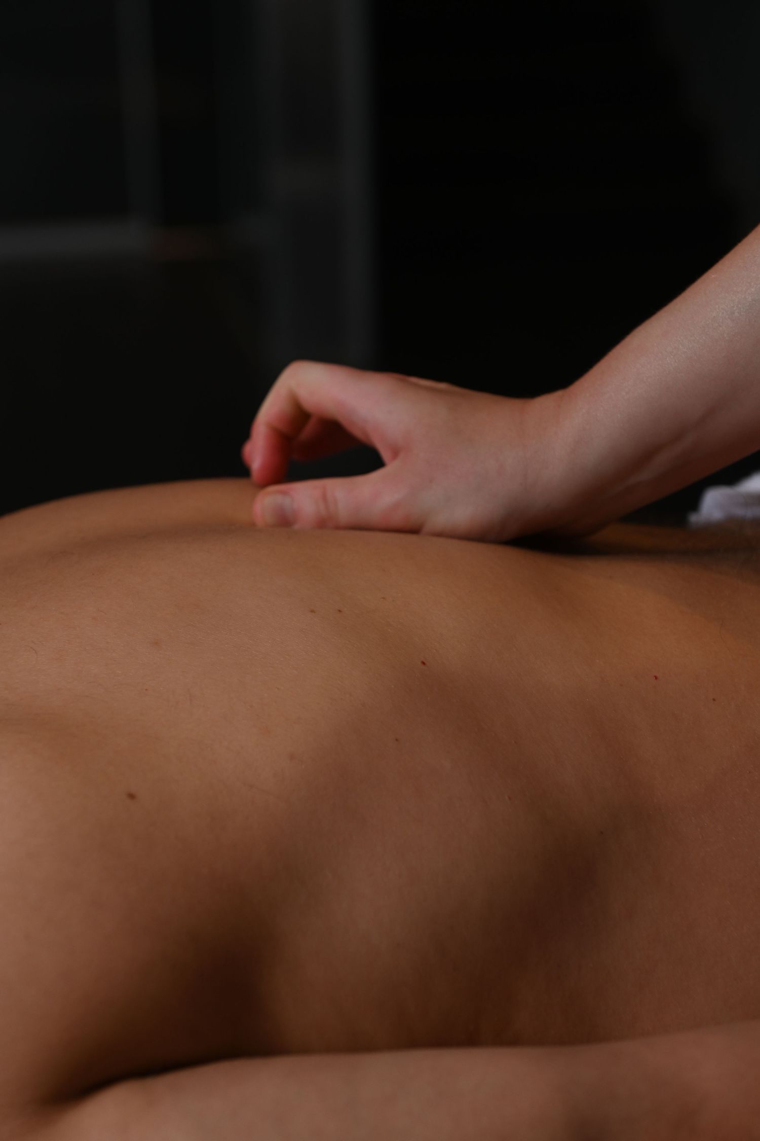 A massage therapist performing acupressure or deep tissue massage on a client's bare back in a spa setting.