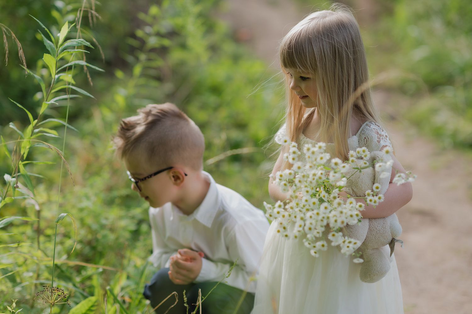 Children walking along a garden path while holding delicate white wildflowers on a sunny summer day.
