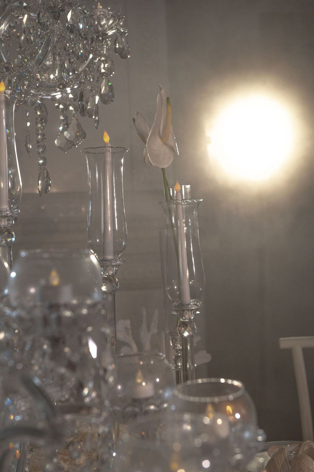 Elegant crystal chandelier and glass candleholders with white candles and a bright spotlight in a formal setting.