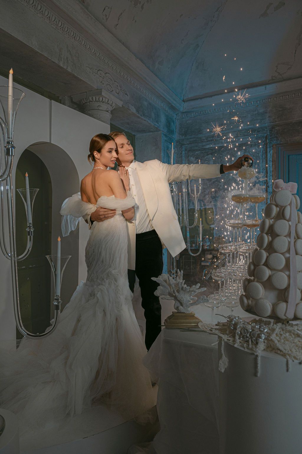 Bride and groom cutting wedding cake with sparklers in elegant white venue, bride in mermaid gown.