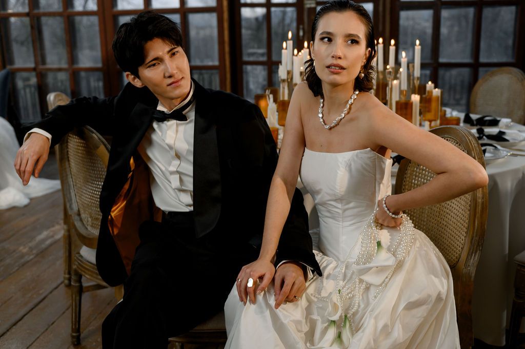 Elegant bride and groom in formal wedding attire seated at a candlelit reception table.