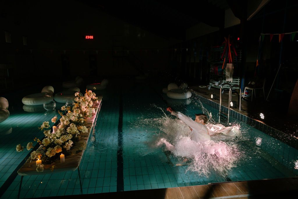 Dark indoor pool with floral arrangements and splashing water during a nighttime event.