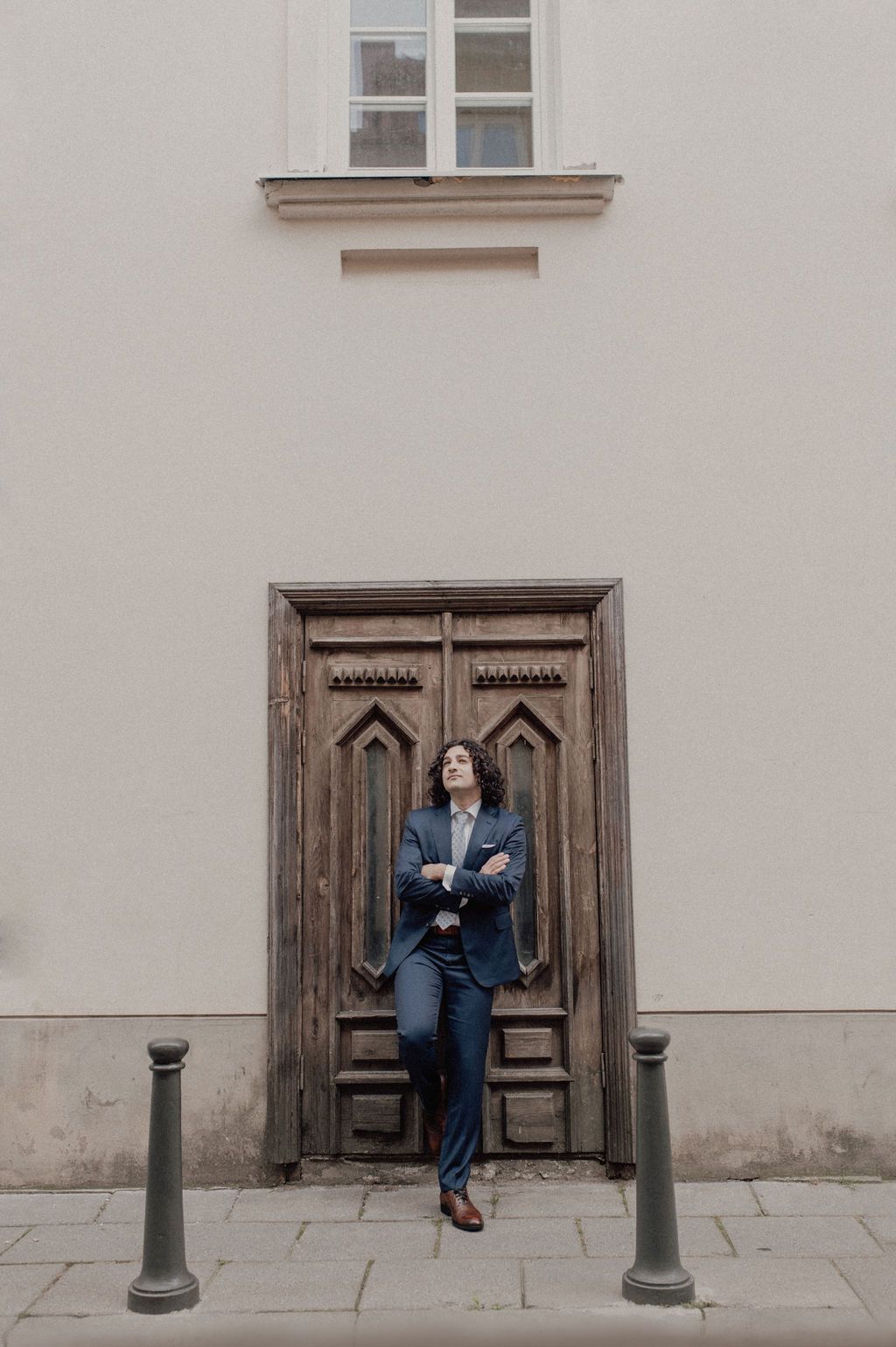 Stylish man in blue suit leaning against ornate wooden door on European city sidewalk.