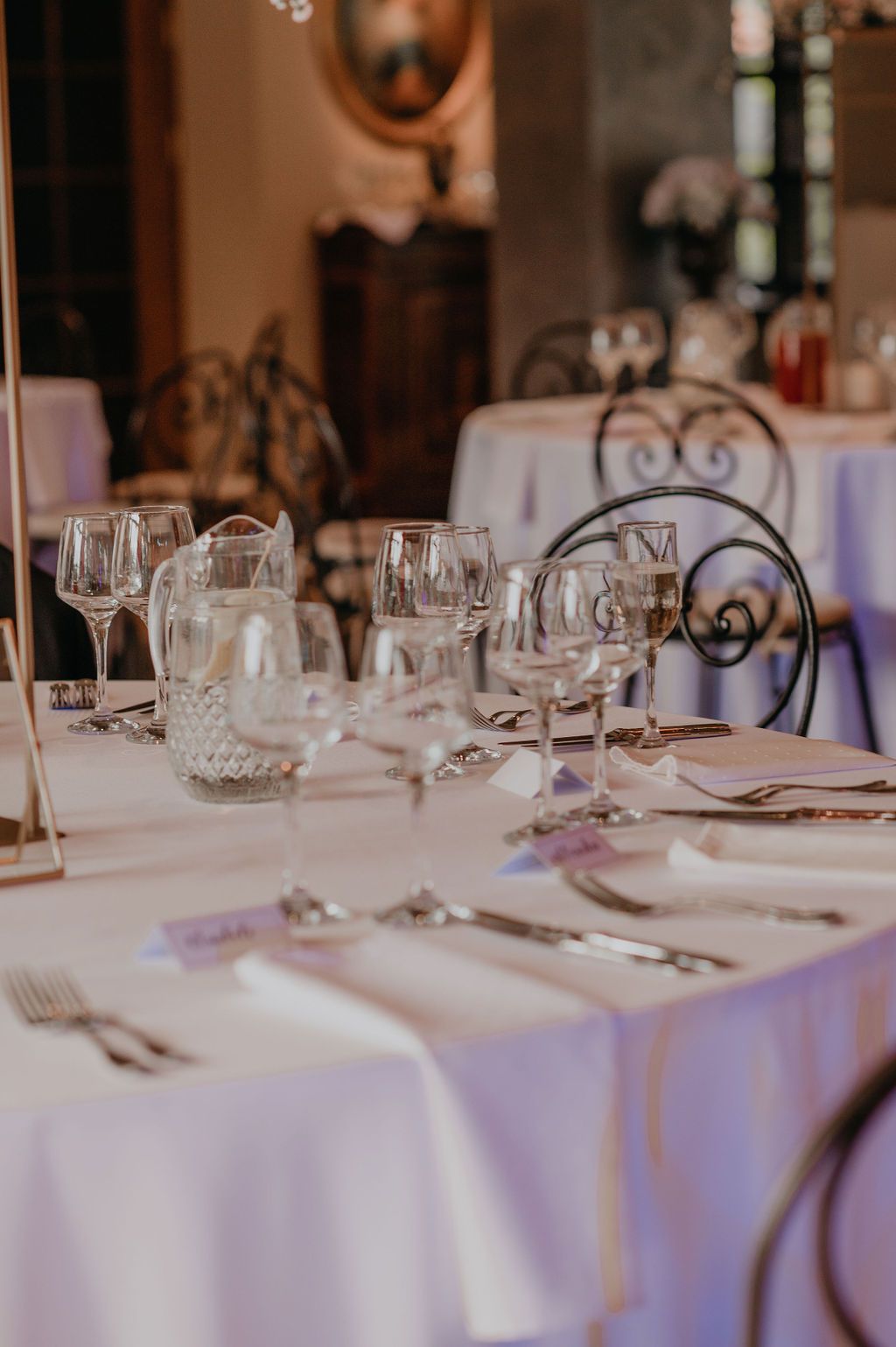 Elegant wedding reception table set with crystal glasses, silverware, and white linens in a classic venue.