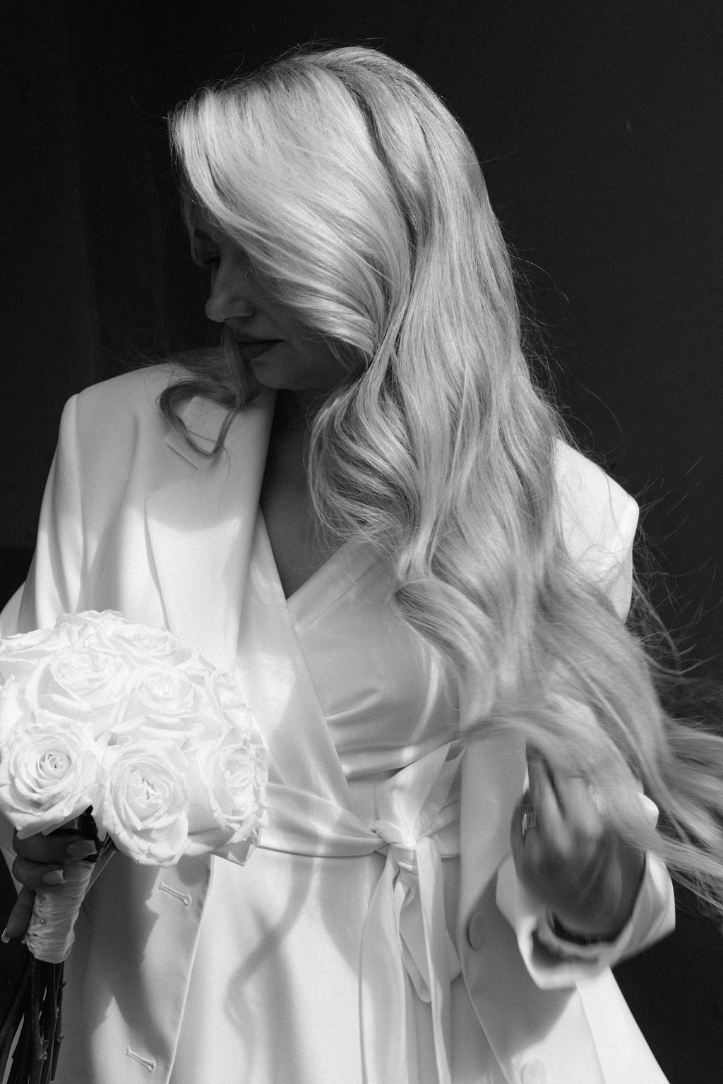 Black and white photo of a blonde bride holding a white rose bouquet in an elegant satin robe.