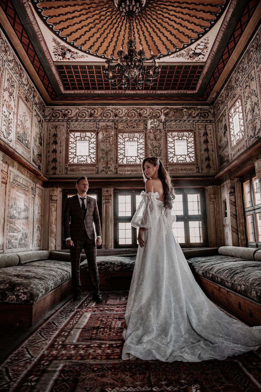 Bride and groom pose in ornate Ottoman-style room with carved wooden ceiling and stained glass windows.