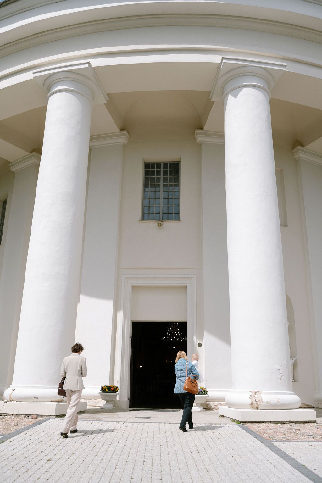 Two people walking toward a grand white neoclassical building entrance with tall columns and a black door.