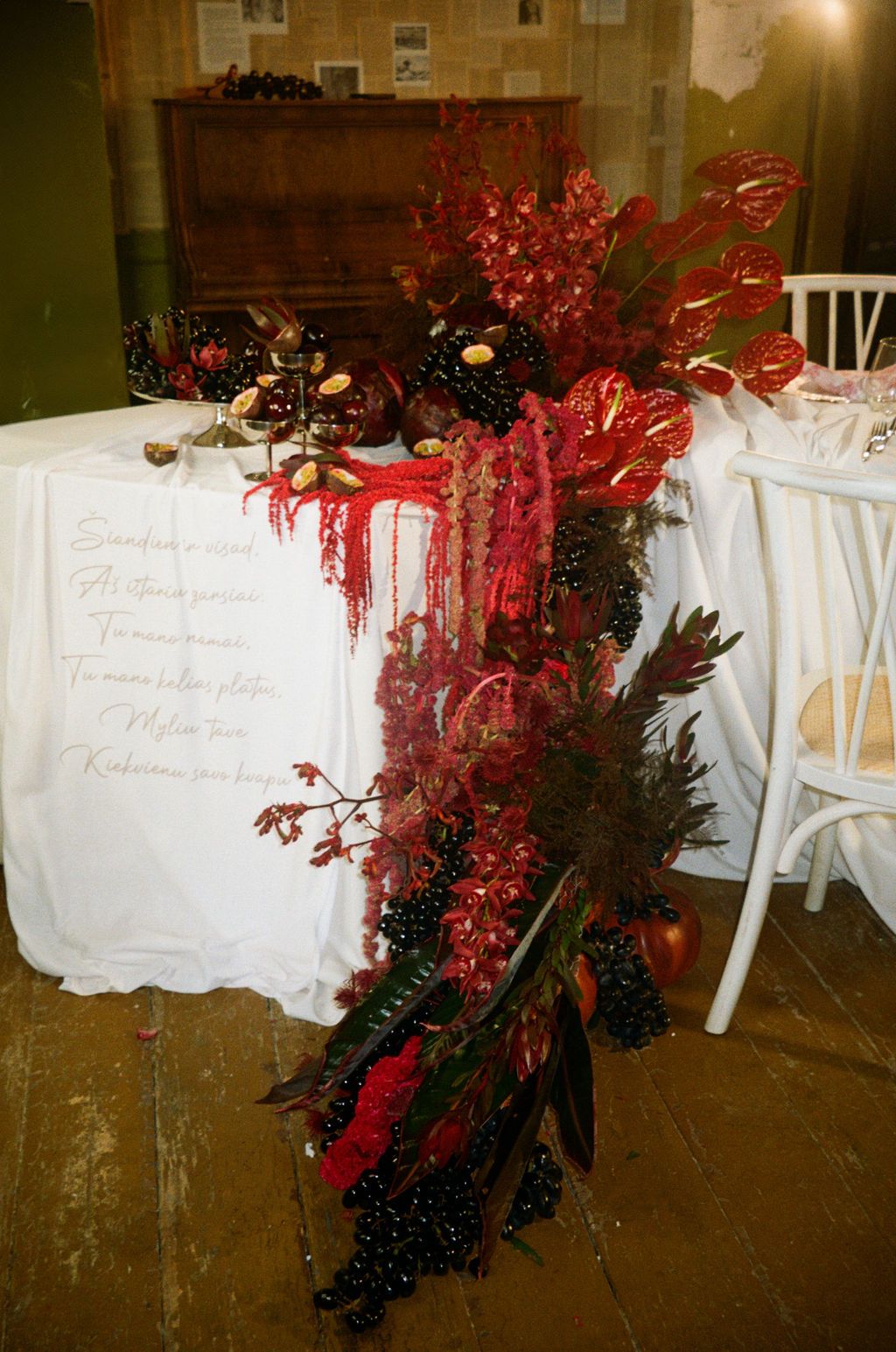Dramatic red floral arrangement with anthuriums and dark berries cascading over a white tablecloth at an elegant event.