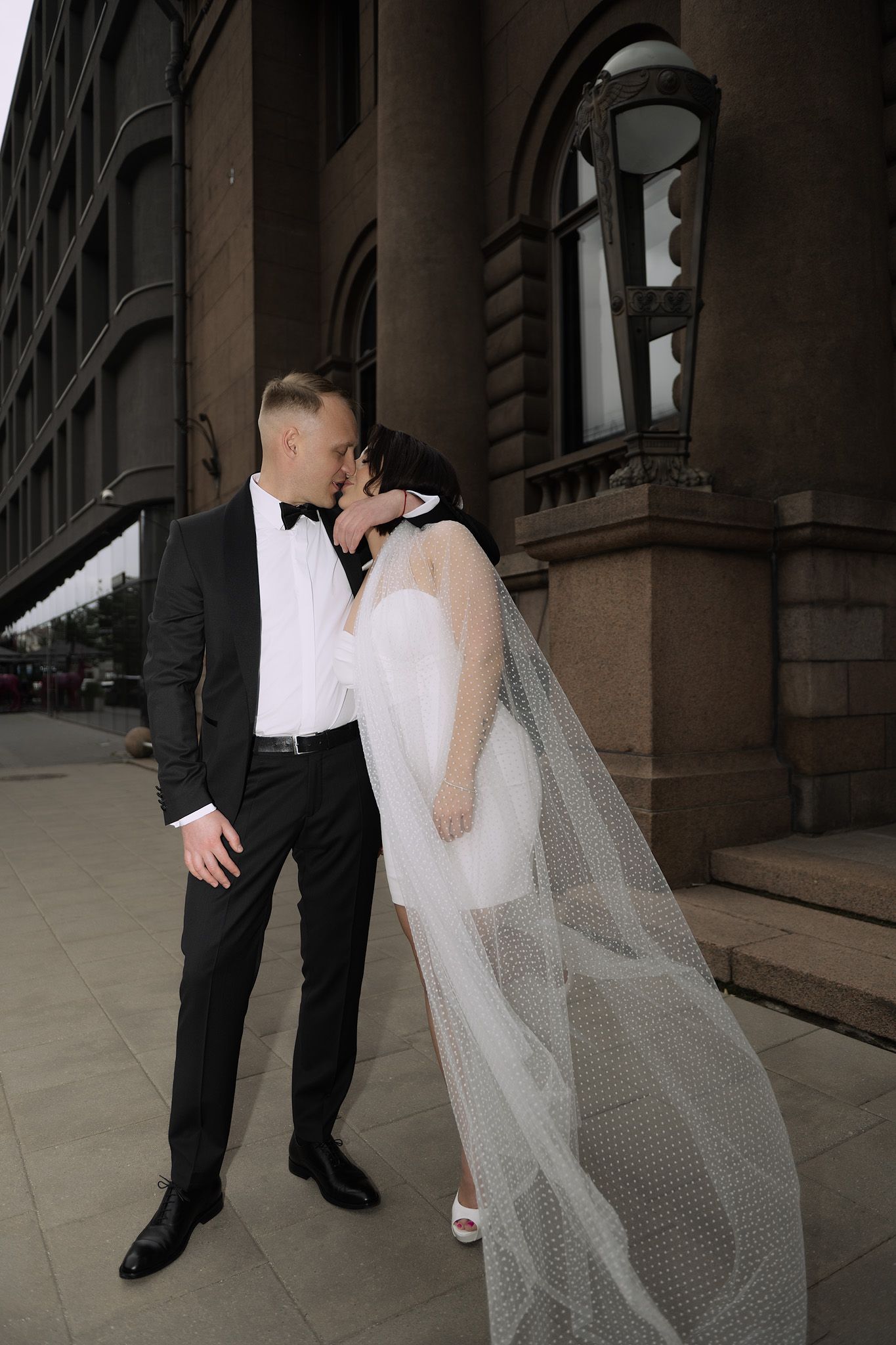 A wedding couple walks together through an elegant stone archway corridor with dramatic lighting.
