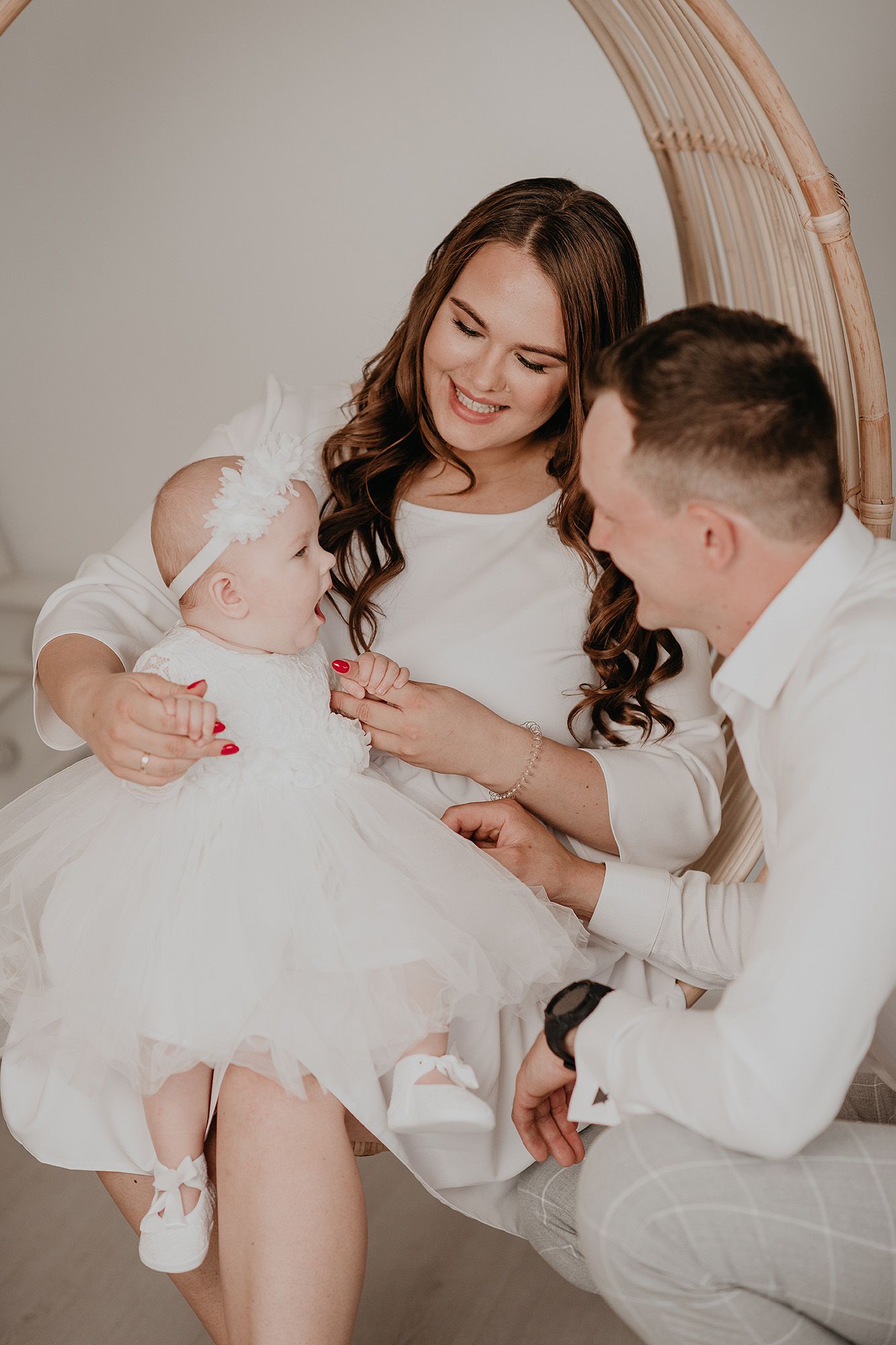 A tender family moment captured in a series of intimate photos showing parents bonding with their newborn baby in white attire.