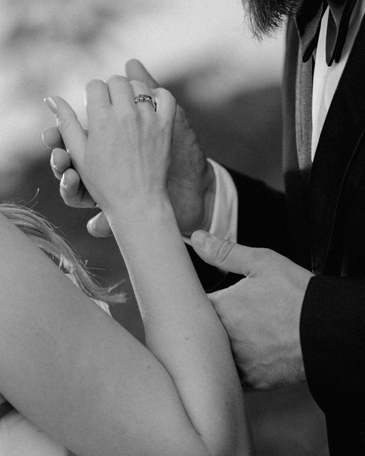 Black and white wedding photo of a groom placing a ring on the bride's finger during the ceremony.