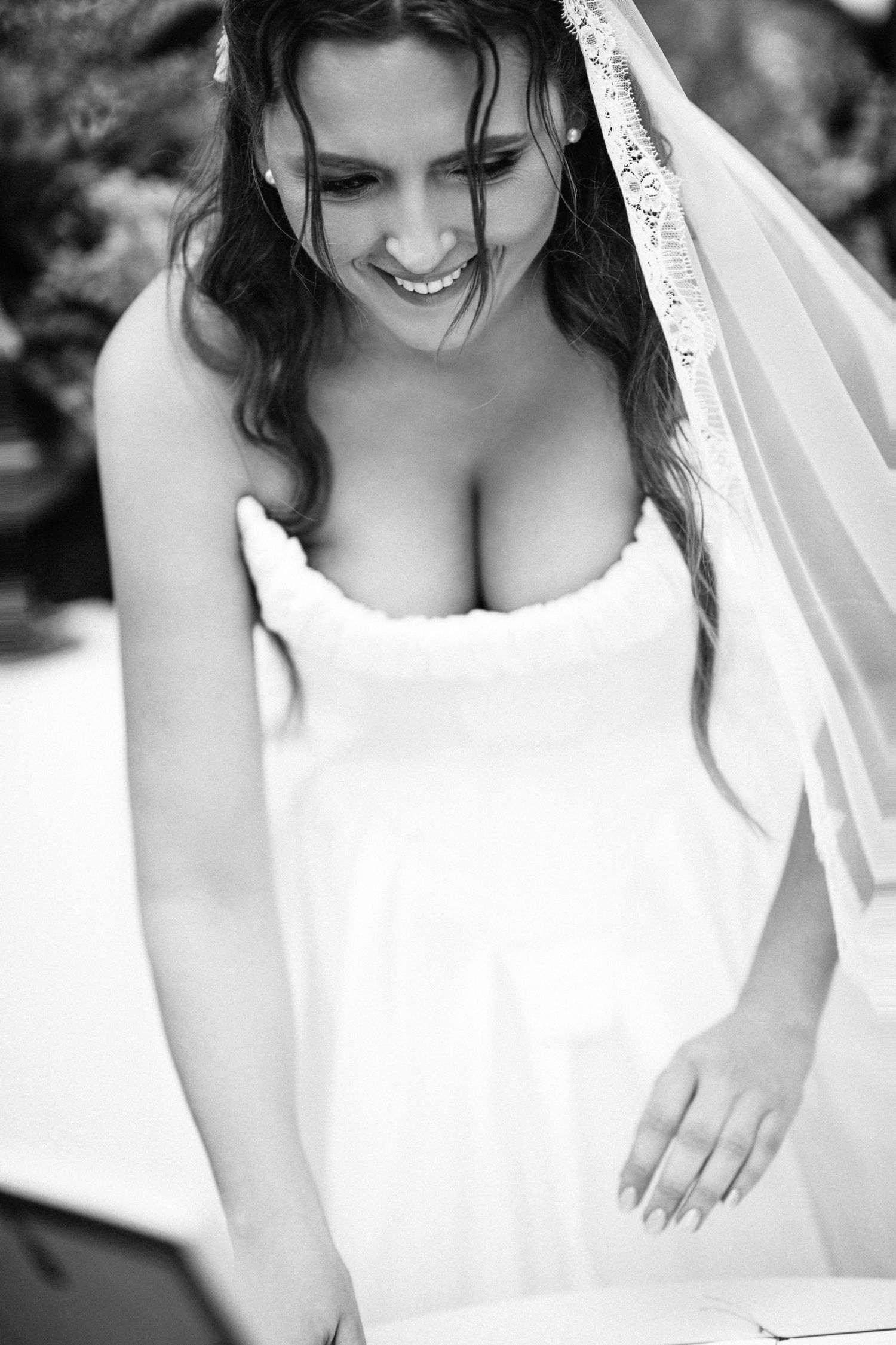 Smiling bride in white strapless gown and veil in black and white wedding photo.