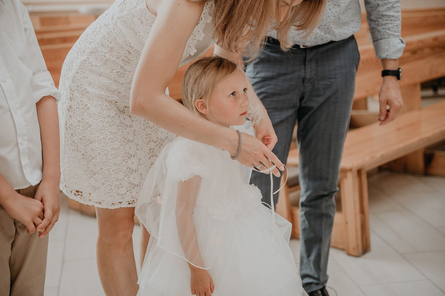 A group of wedding guests in white and gray attire stand in a line during a church ceremony.