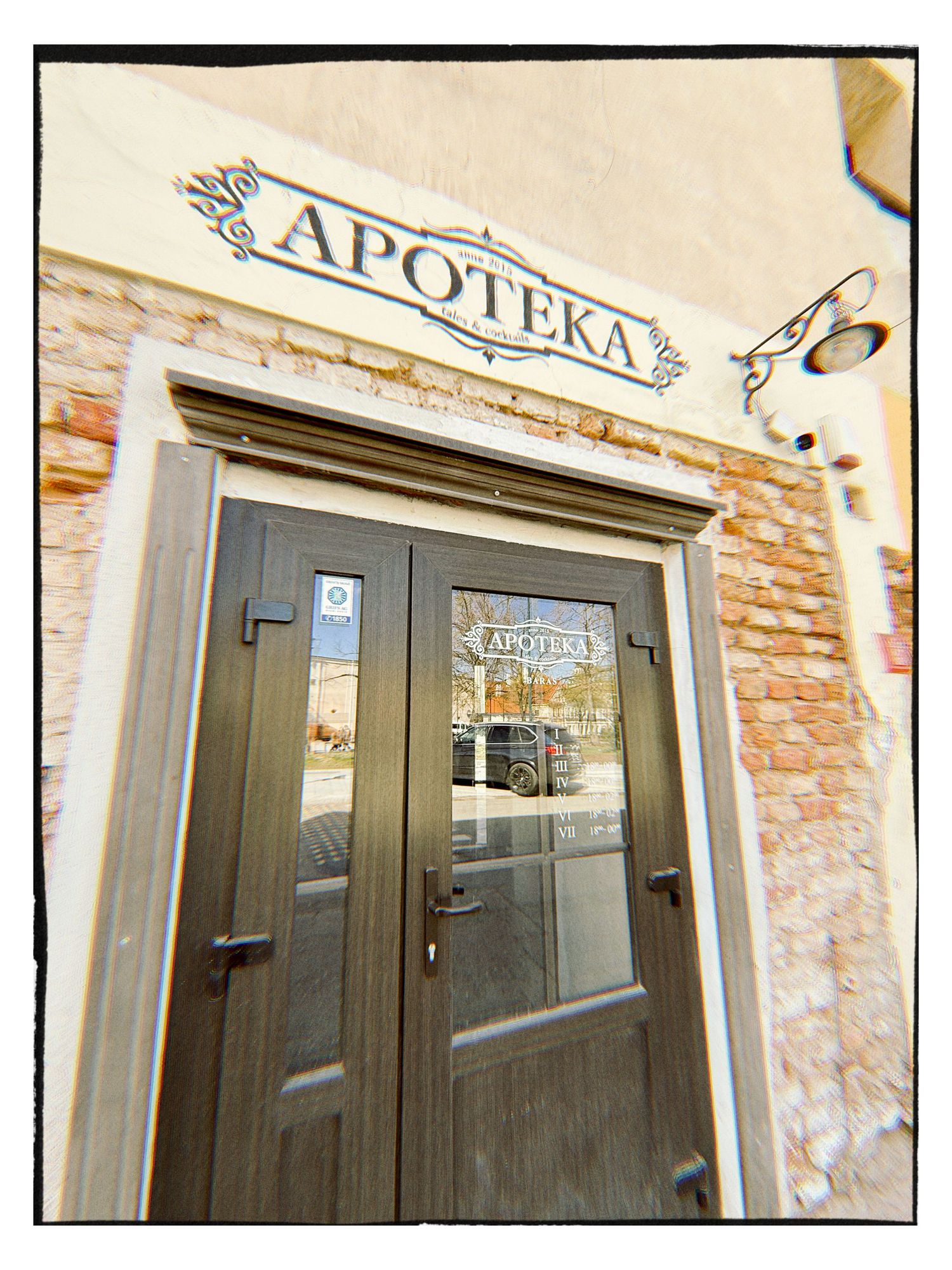 Vintage brick building entrance with dark wooden double doors and decorative APOTEKA pharmacy sign above.
