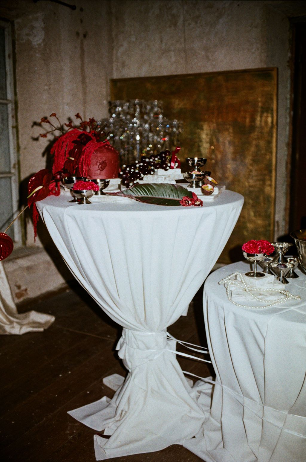 Elegant cocktail table with white draping adorned with red floral arrangements and festive decor in a rustic venue.