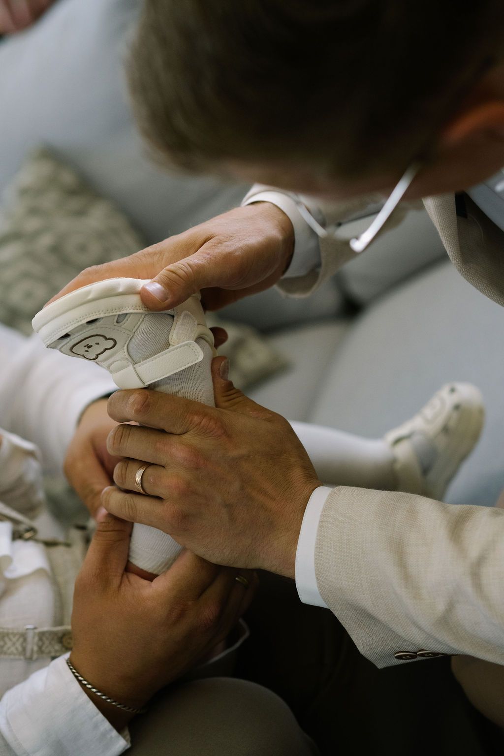 Adult hands carefully putting white baby shoes on an infant during a christening ceremony.