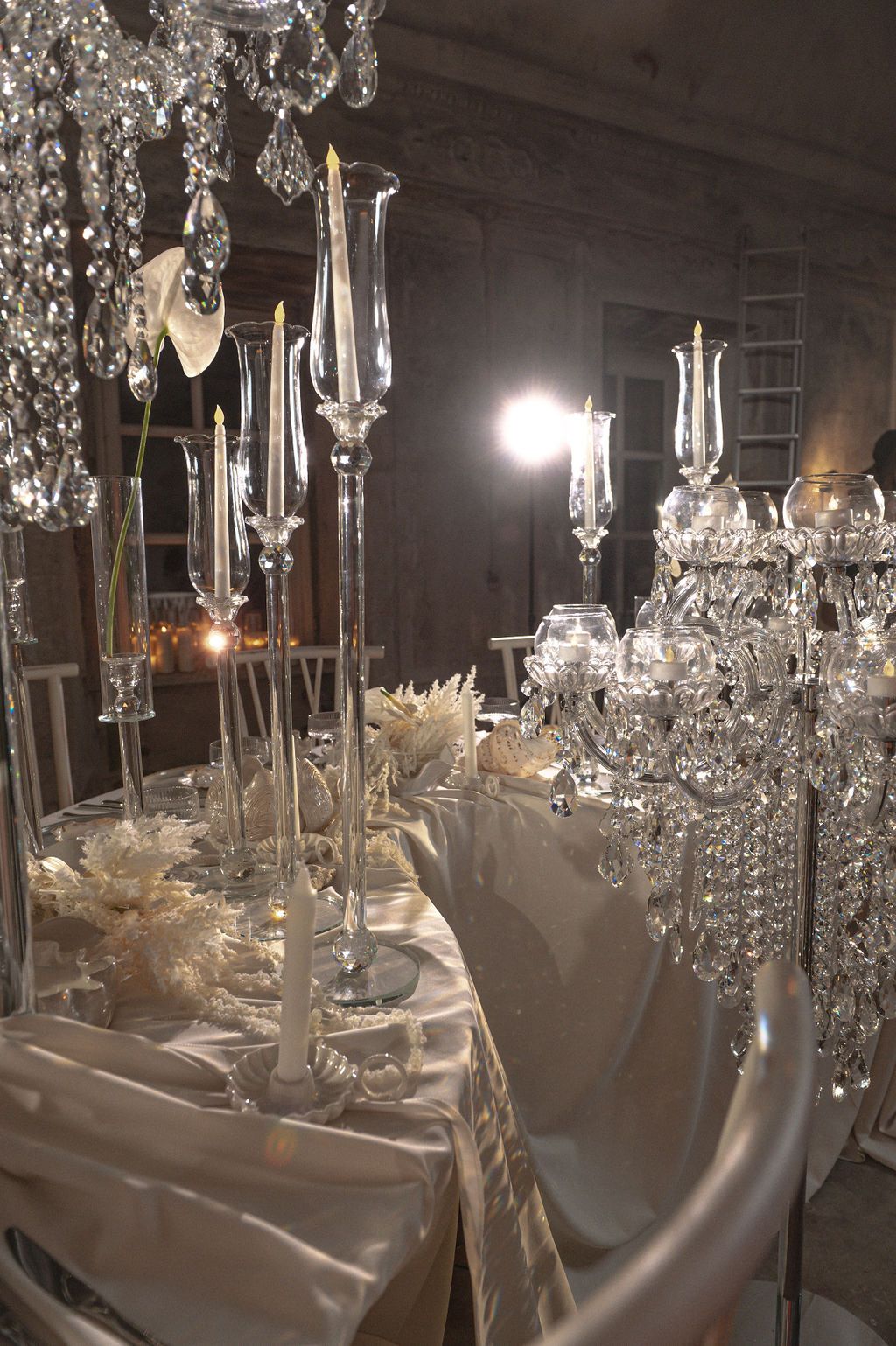 Elegant crystal candelabras and tall glass candlesticks adorn a luxurious white satin wedding reception table.