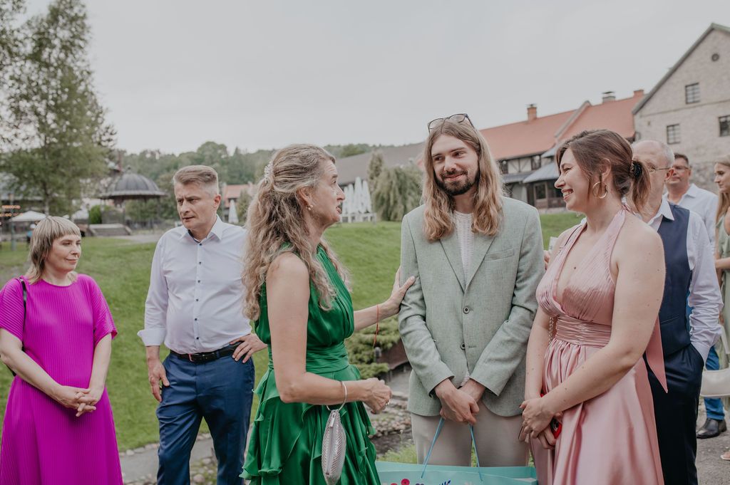 Elegant outdoor wedding gathering with guests in formal attire including green and pink dresses on a cloudy day.
