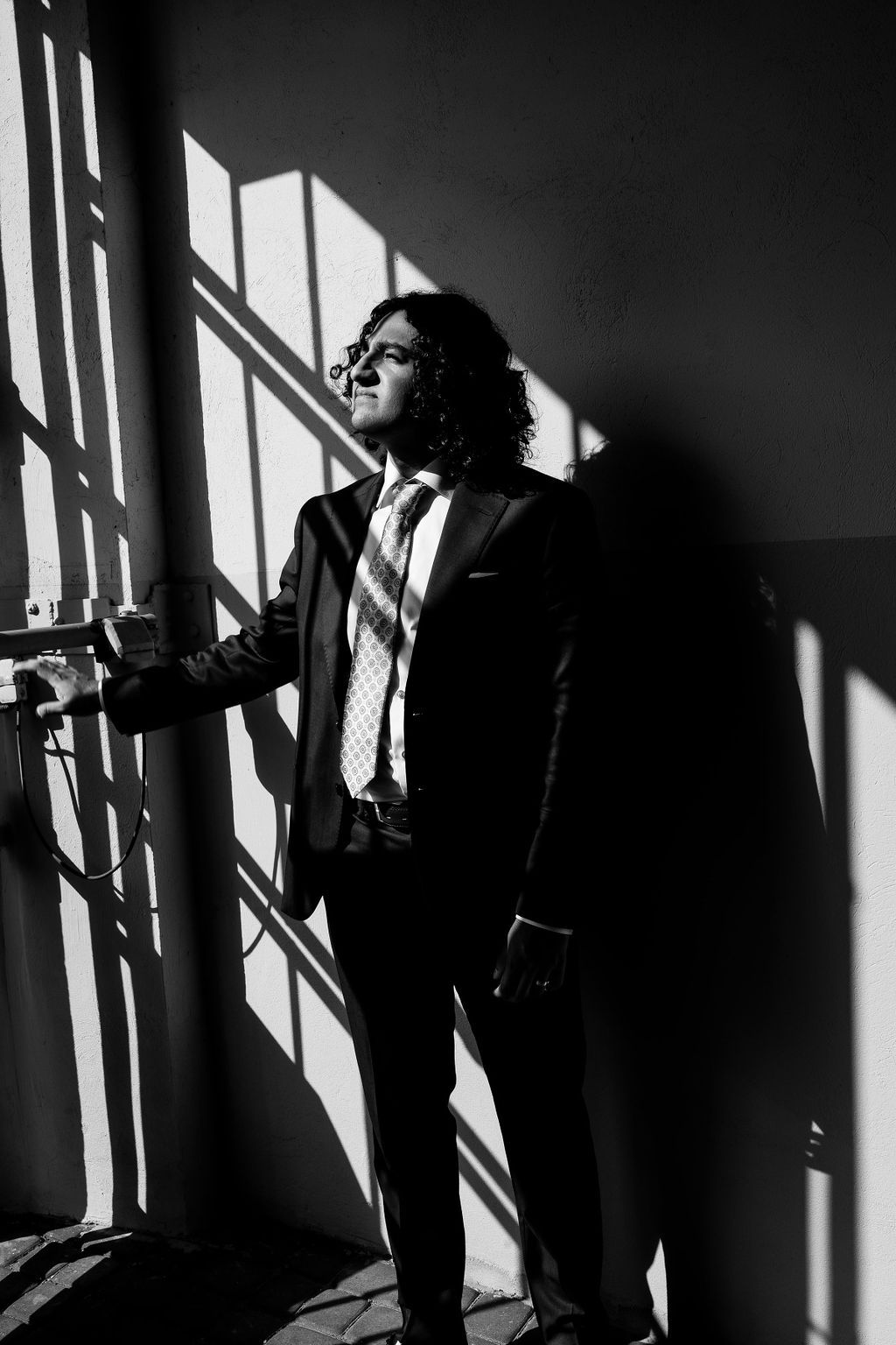 Stylish man in black suit and striped tie standing in dramatic light and shadow in black and white photo.