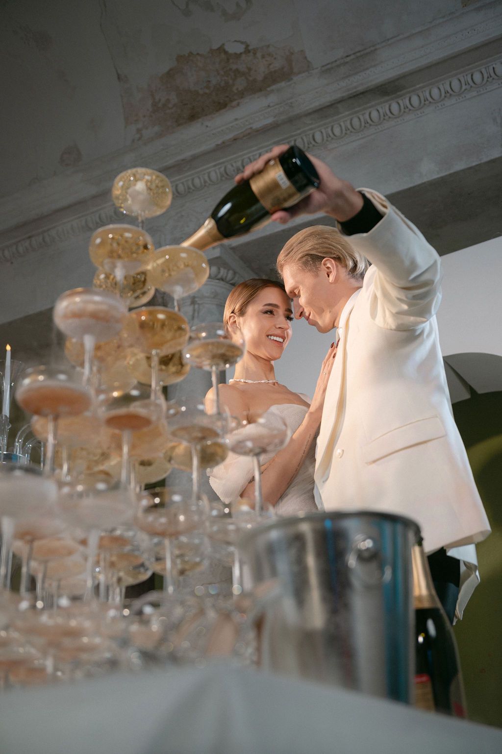 Bride and groom pouring champagne tower at wedding reception in elegant venue.