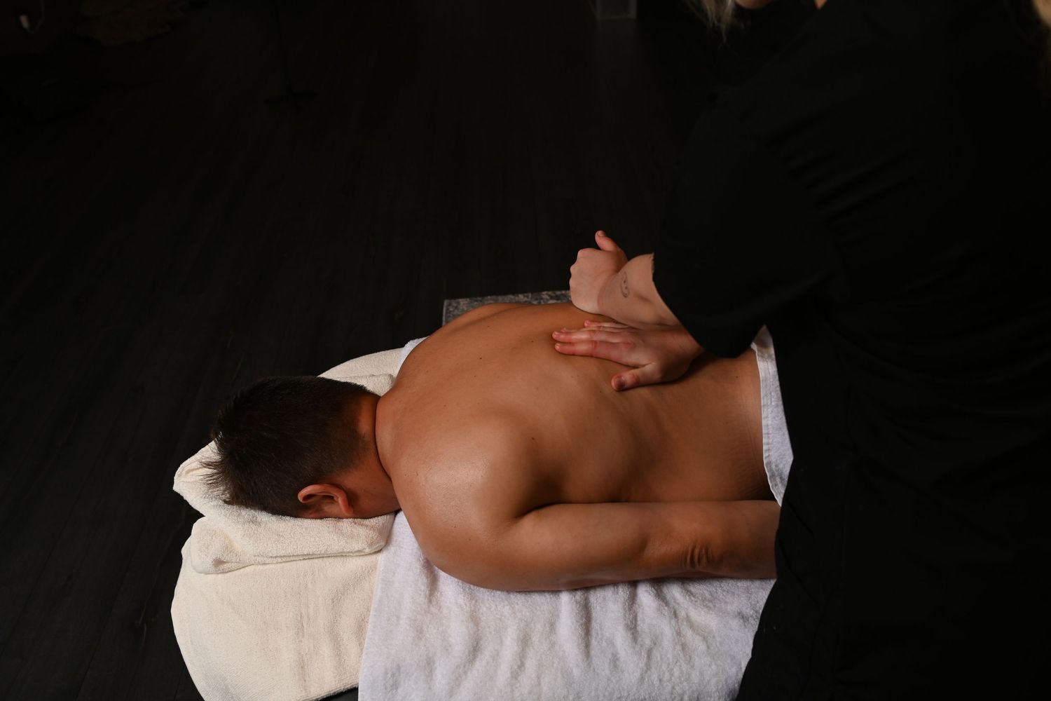 Professional massage therapist performing a relaxing back massage on a male client lying on a white towel.