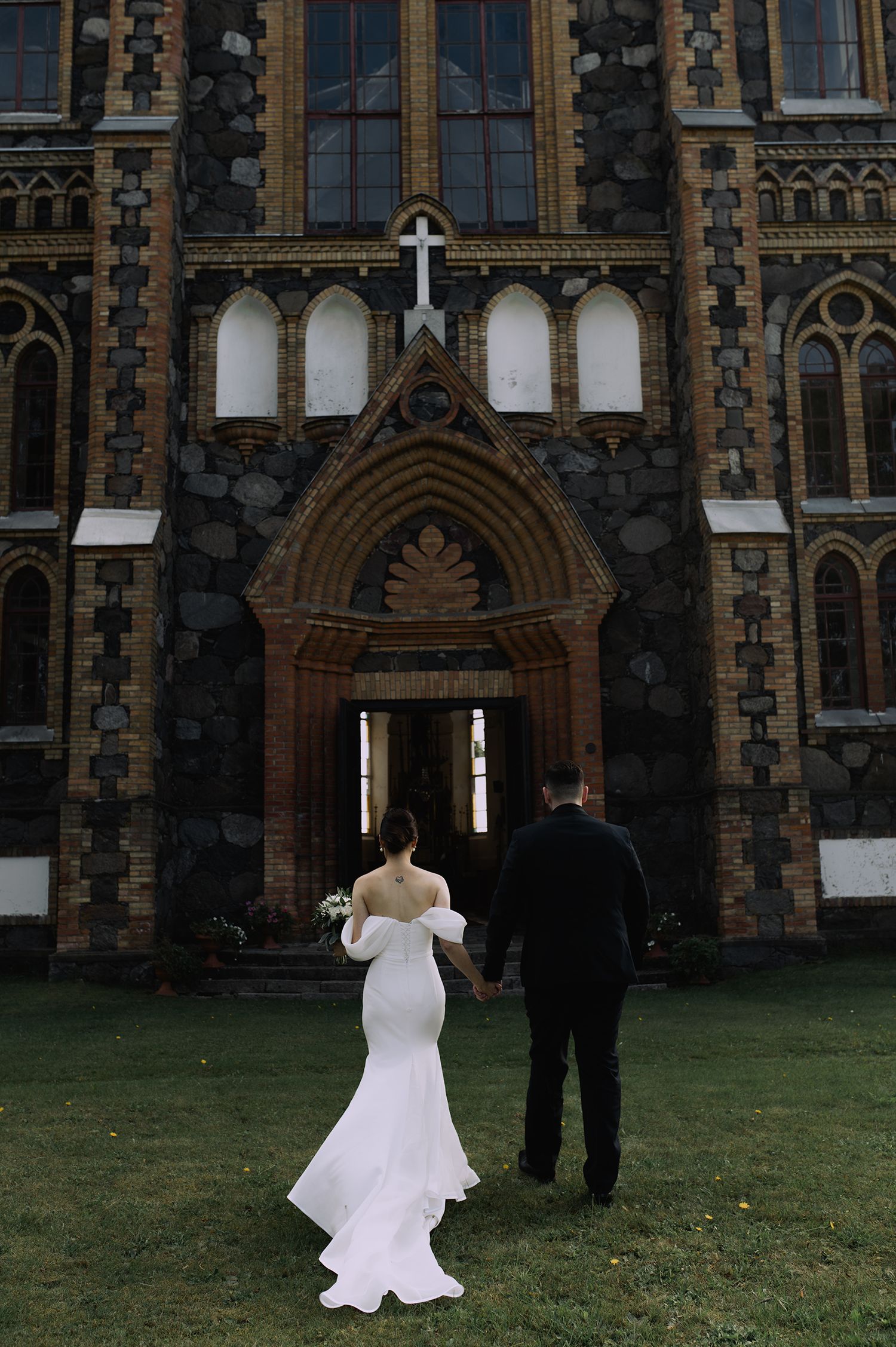 A bride in a white wedding dress spins and twirls on the lawn in front of a Gothic-style church building.