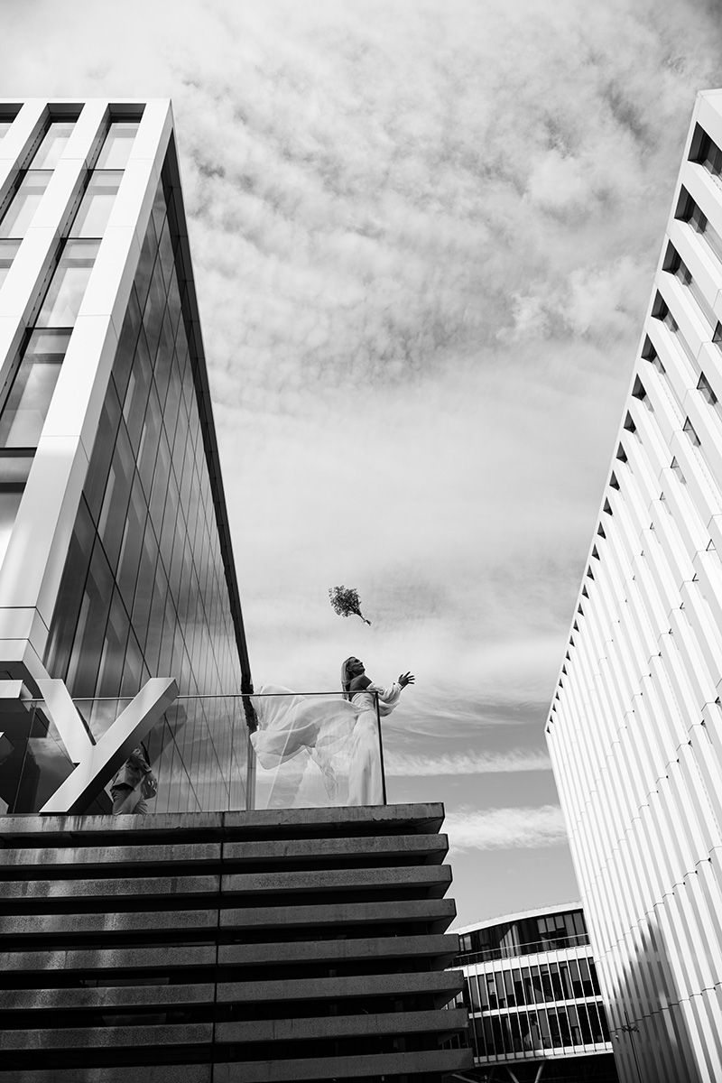 Black and white architectural photograph showing modern buildings with geometric lines and wispy clouds in the sky.