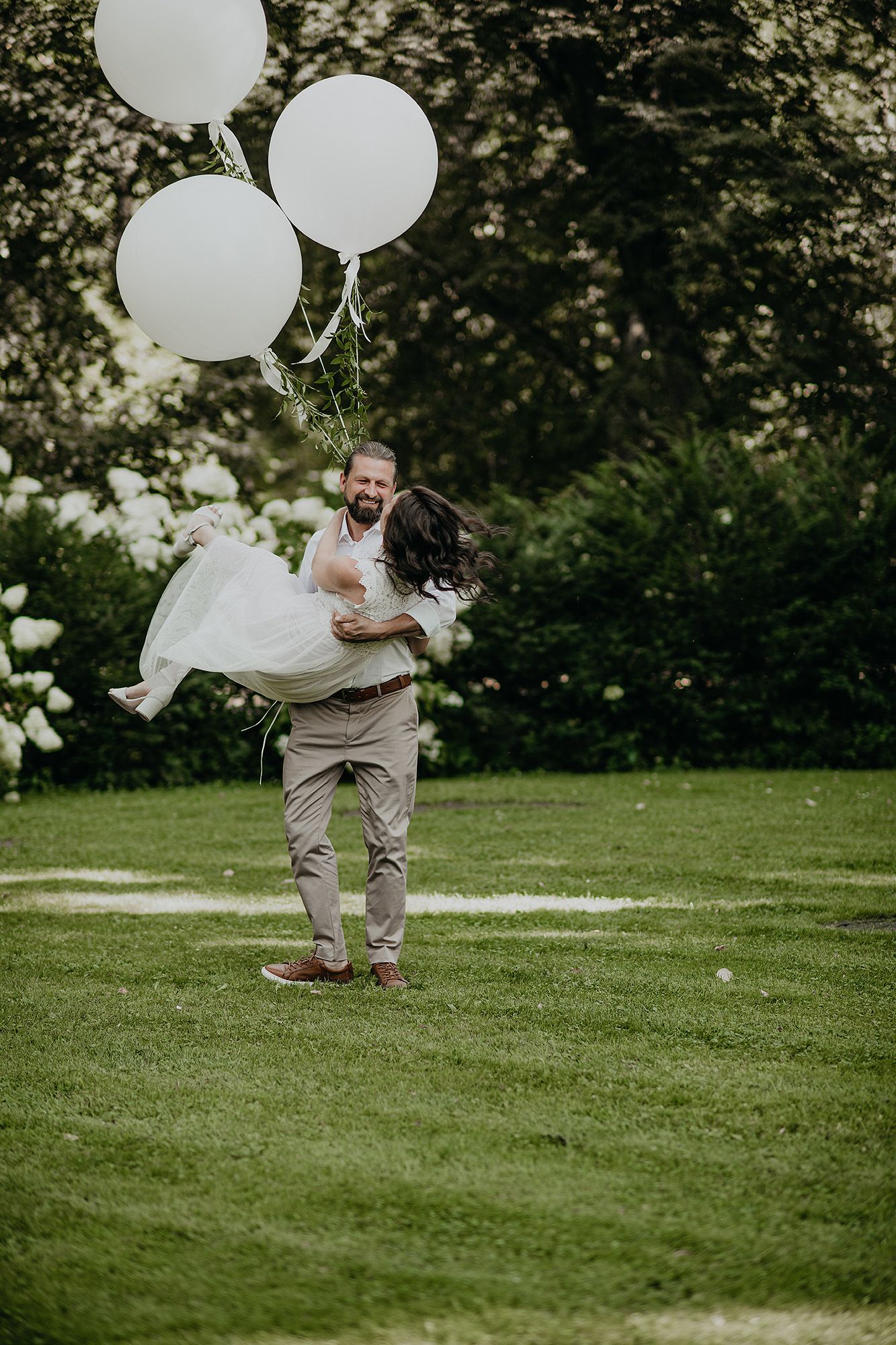 Joyful moment captured in a garden with white balloons and a celebratory twirl on green grass.