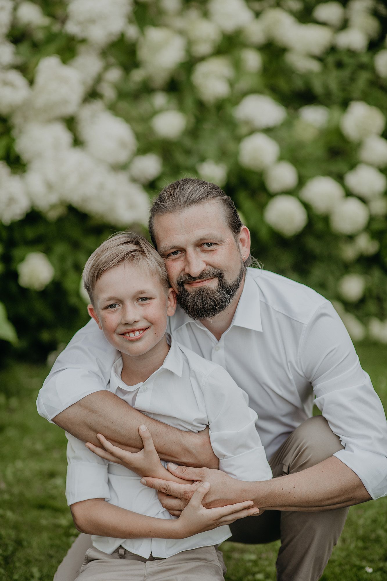 A heartwarming outdoor portrait of a parent and child in matching white shirts against a backdrop of white flowers.