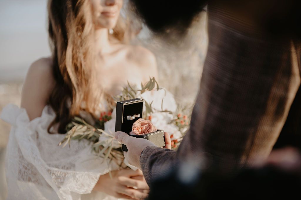 Close-up of bride holding floral bouquet and ring box during intimate outdoor wedding ceremony.