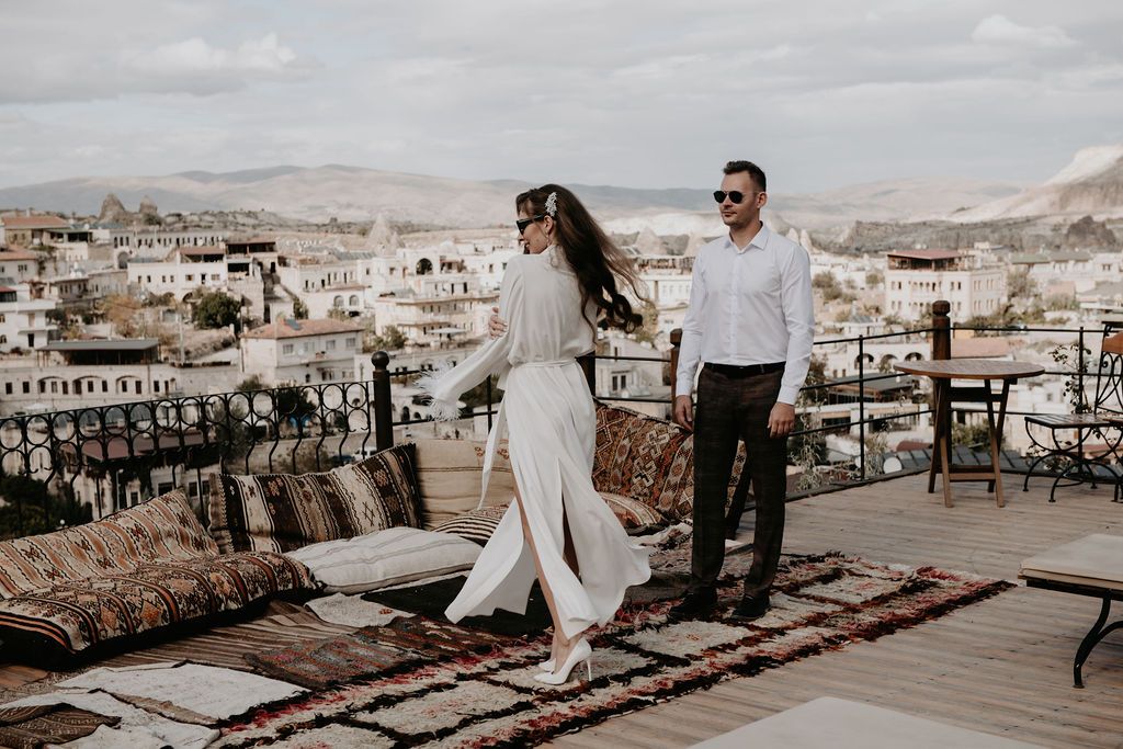 Couple in wedding attire walking on a rooftop terrace in Cappadocia, Turkey, with scenic town views.