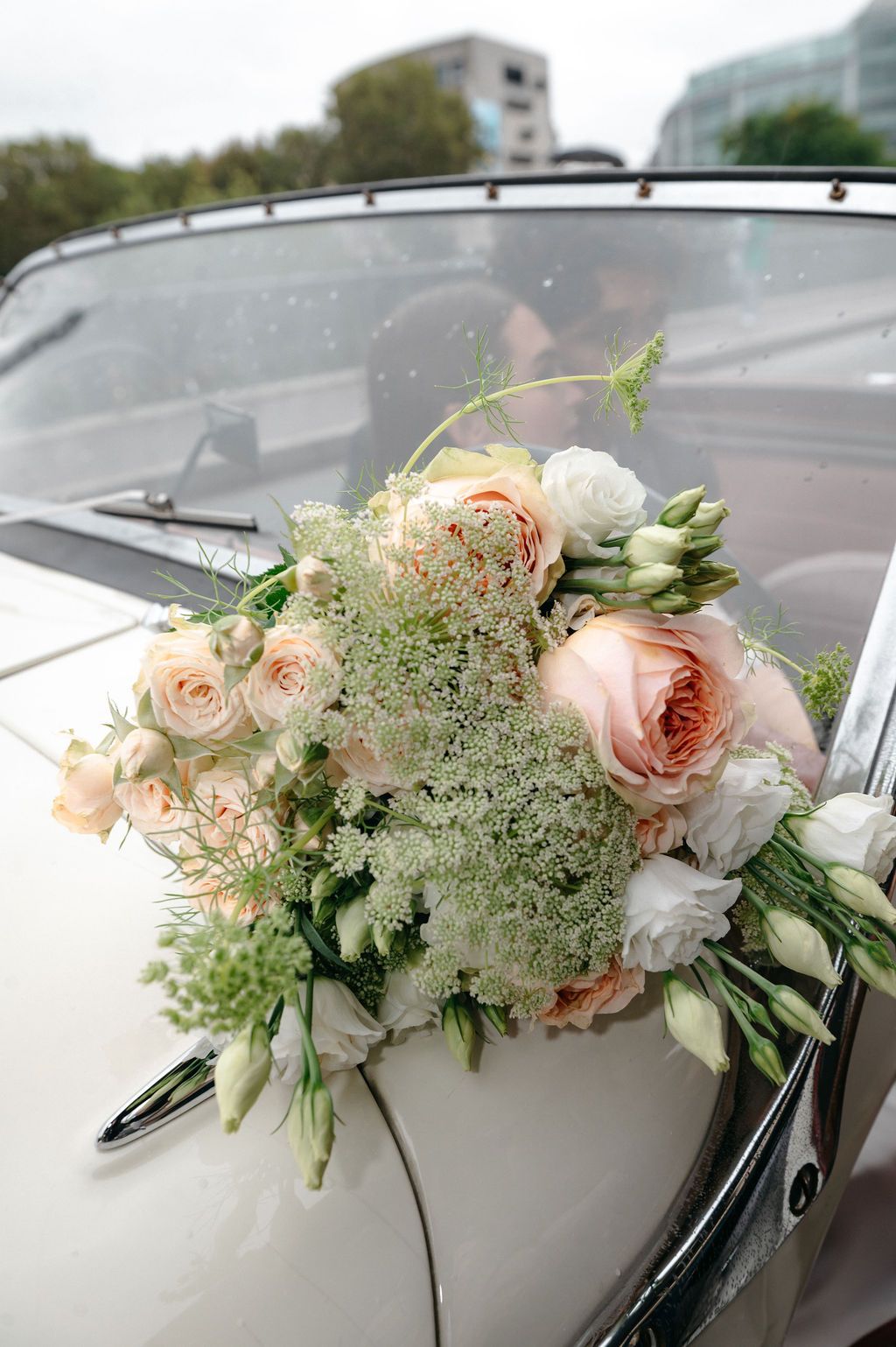 Elegant wedding bouquet of peach roses and white flowers resting on a classic white vintage car door.