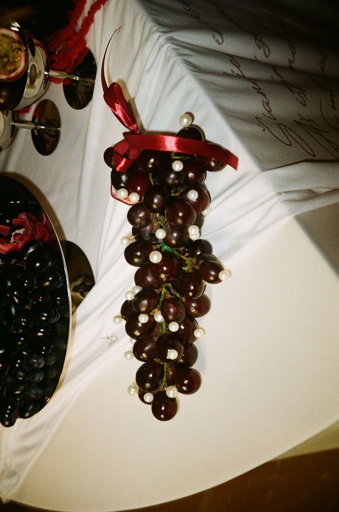 Decorative bunch of dark red grapes with pearl accents and red ribbon bow displayed on white tablecloth.