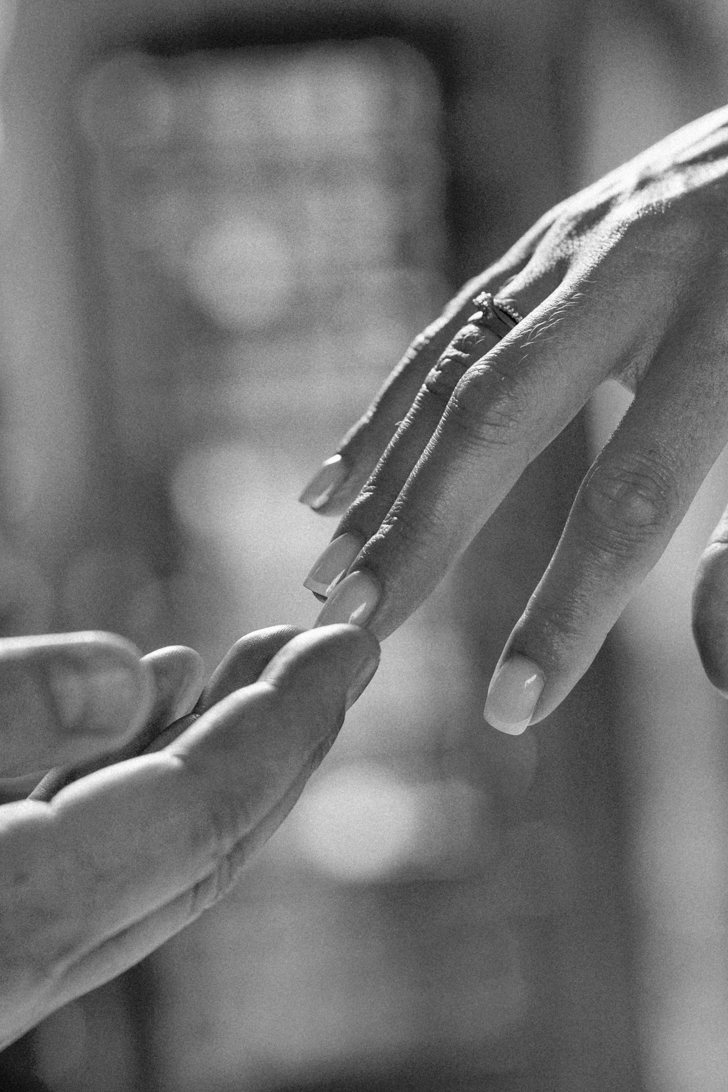 Black and white close-up of a man's hand gently holding a woman's hand with a ring on her finger during a proposal or wedding moment.
