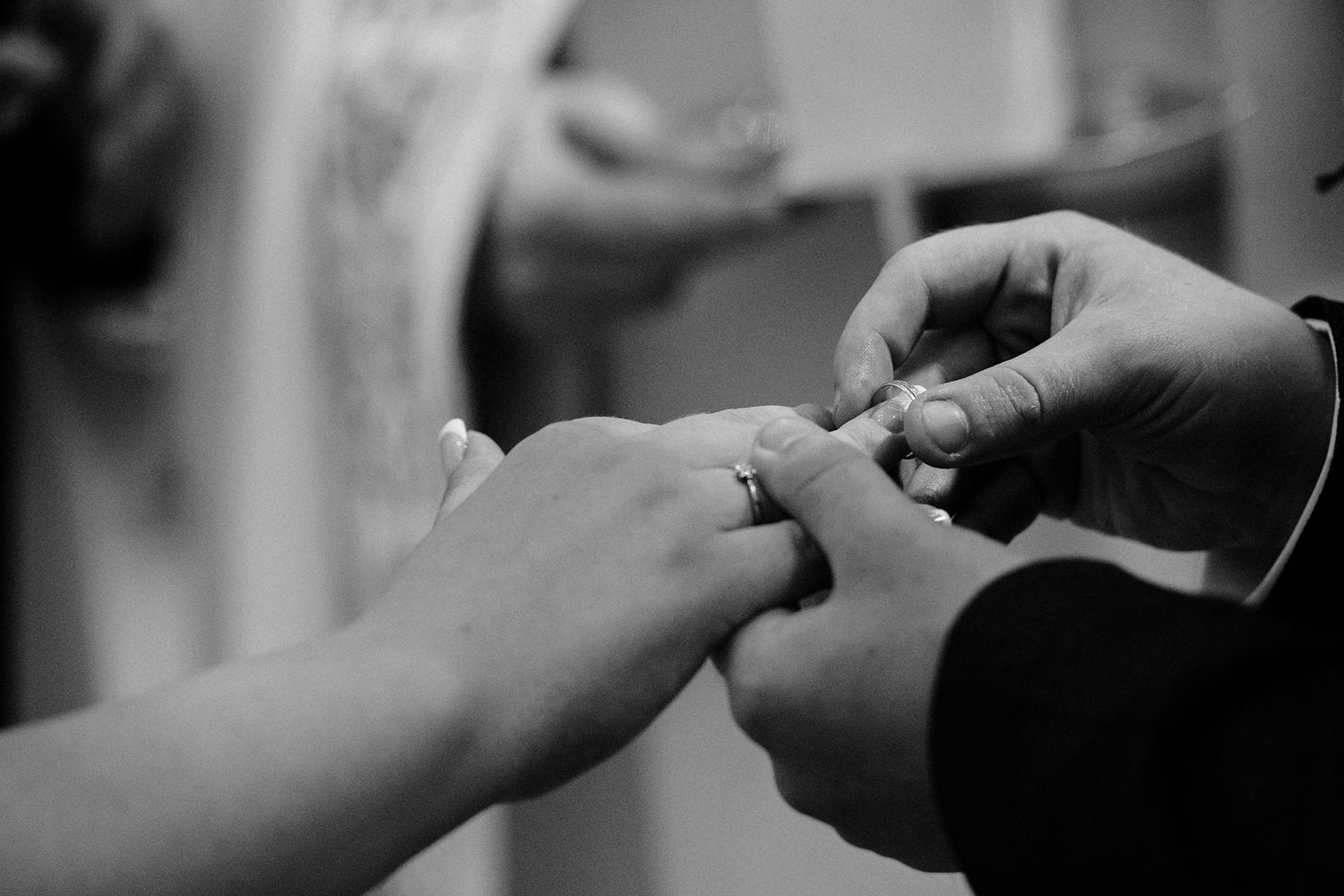 A black and white close-up photo of hands exchanging wedding rings during a ceremony.