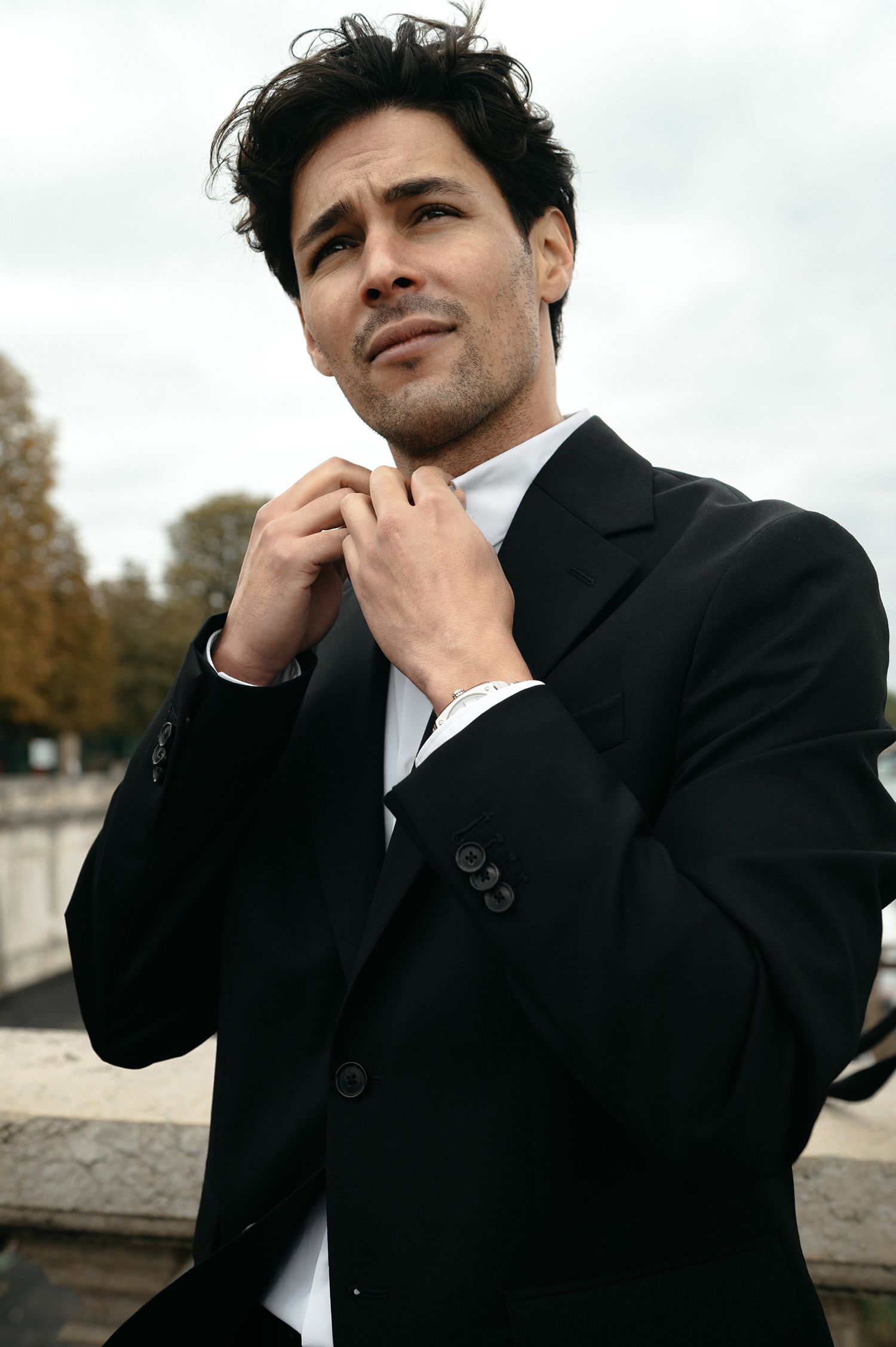 A man in a black suit poses thoughtfully against an outdoor backdrop in a series of professional portraits.