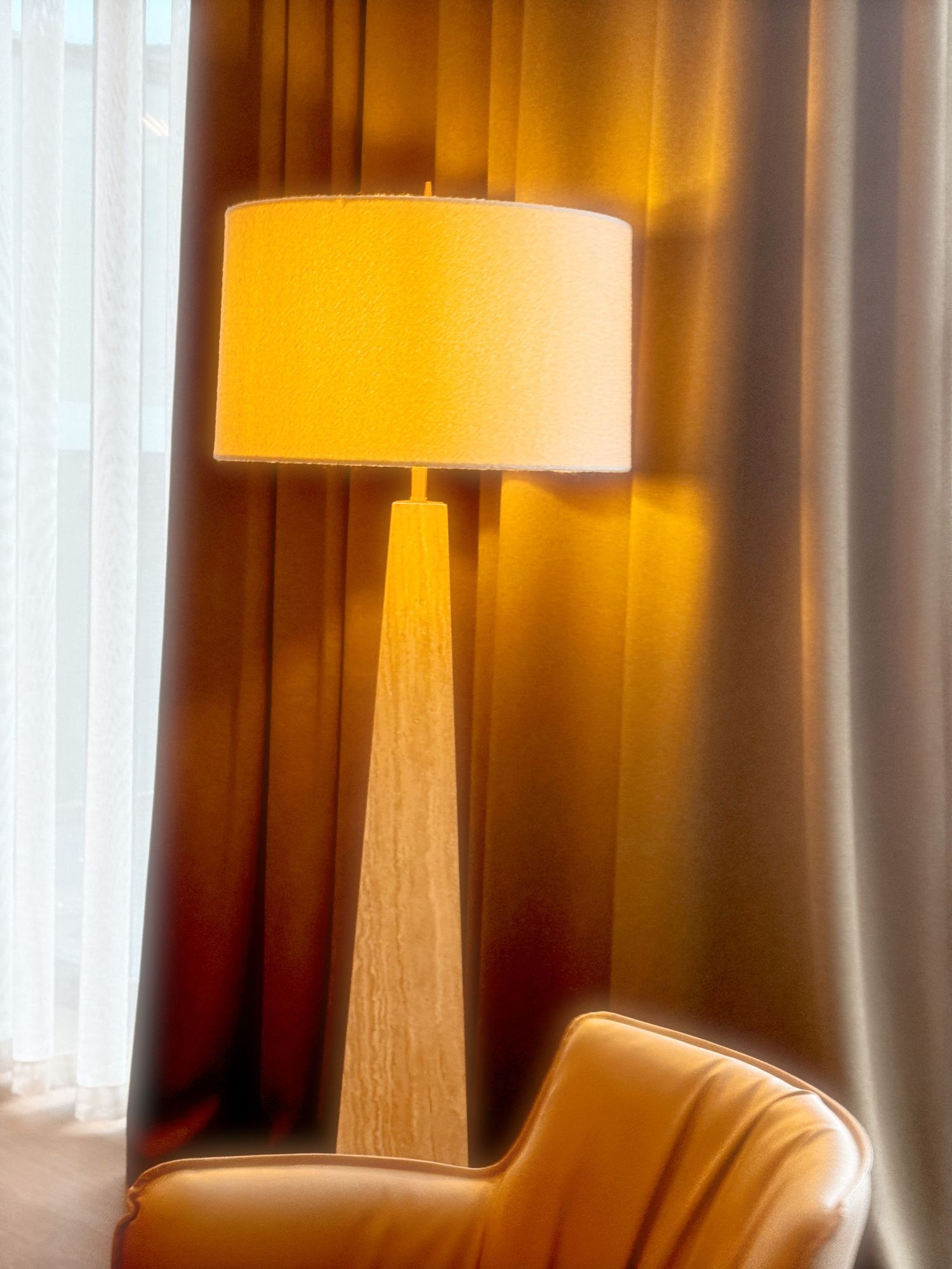 Modern hotel room interior with warm lighting, tall table lamps, and floor-to-ceiling curtains creating an inviting ambiance.