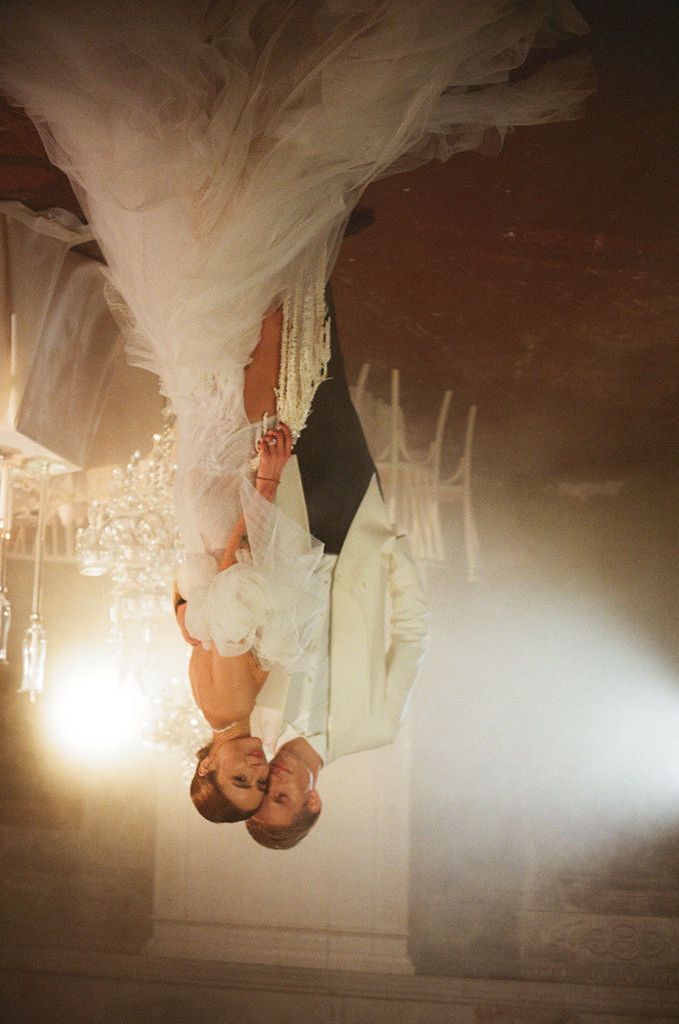 Upside-down wedding photo of bride and groom sharing a romantic moment in an elegant chandelier-lit venue.