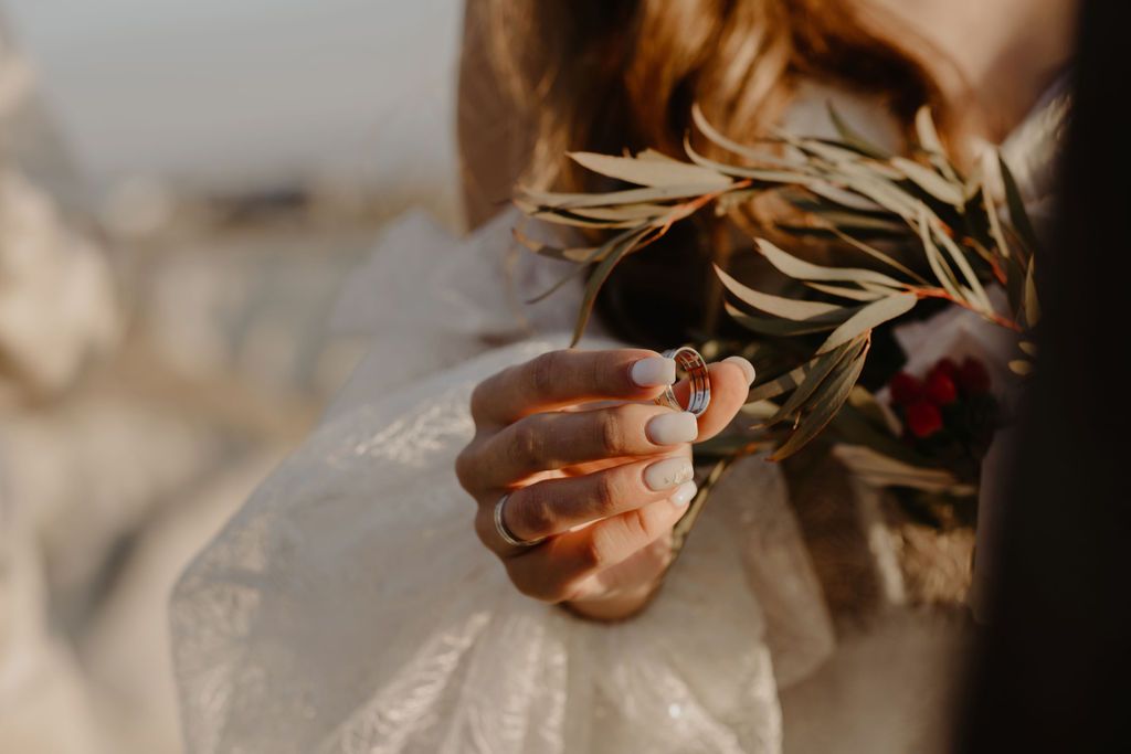 Close-up of bride holding olive leaf crown with elegant engagement ring visible on her finger.