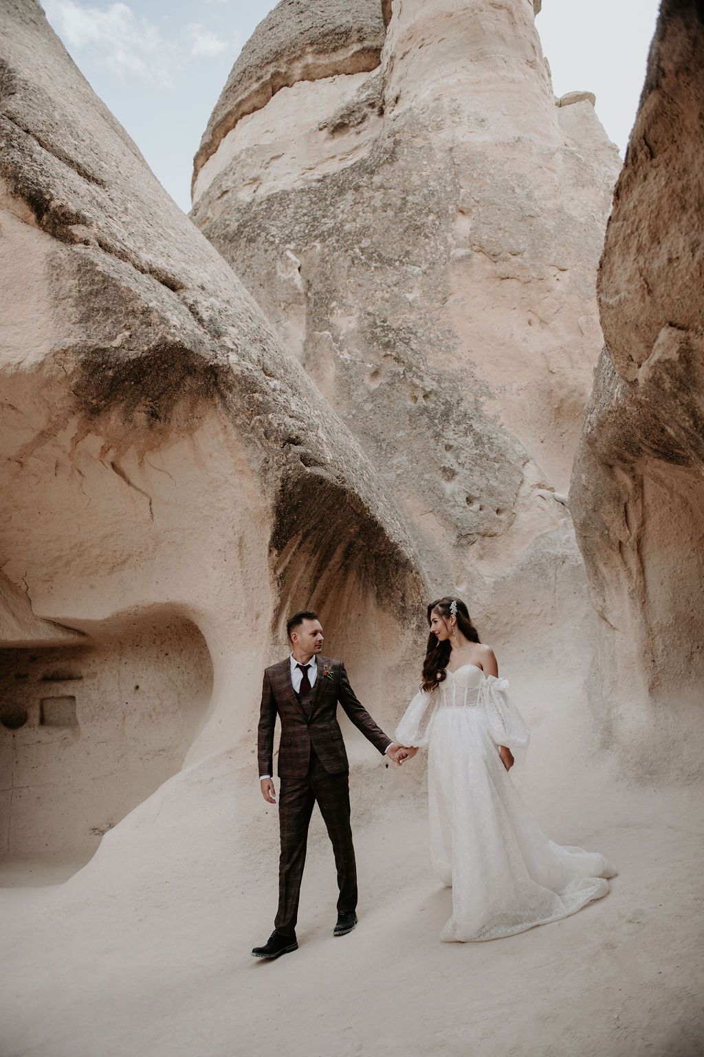 Bride and groom hold hands among towering sandstone rock formations in Cappadocia, Turkey, during their wedding shoot.