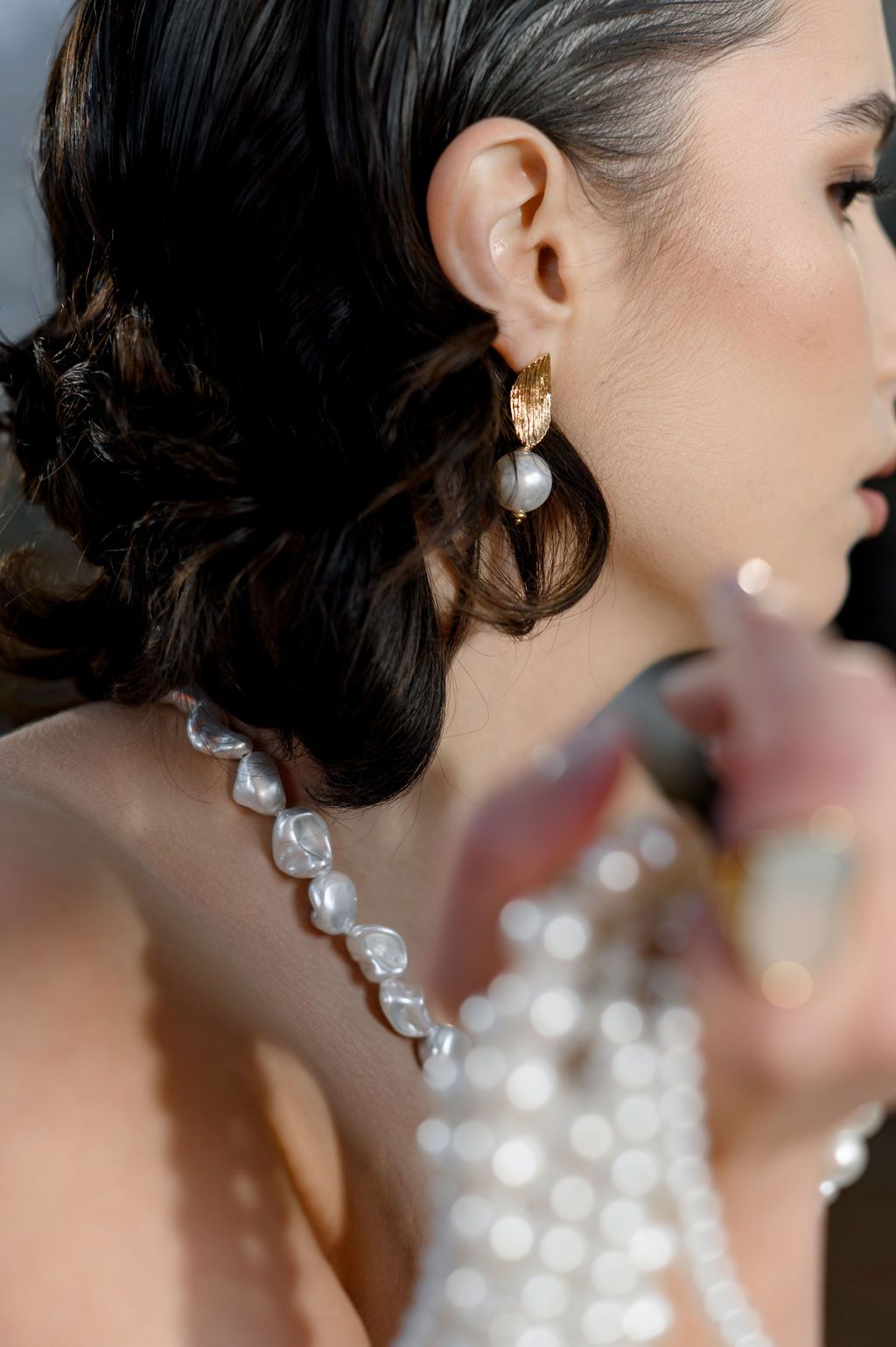 Close-up of a bride wearing gold pearl drop earrings and a pearl necklace with dark hair in an elegant updo.