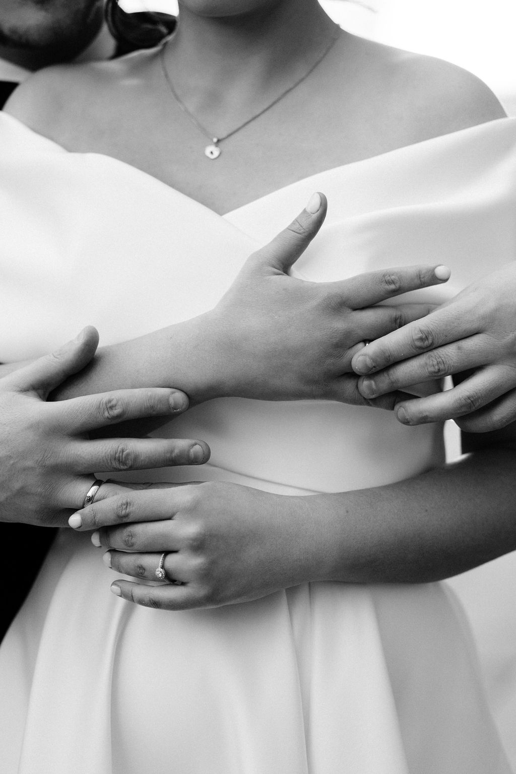 Black and white photo of newlyweds embracing, showing wedding rings on their hands, bride in white dress.