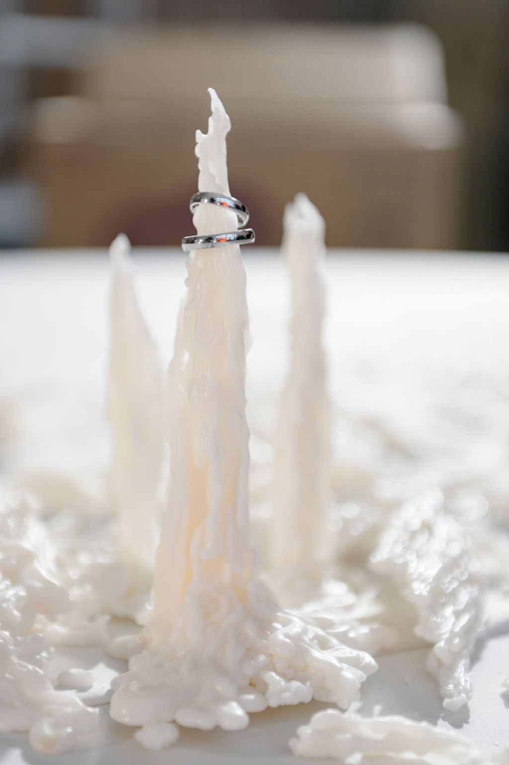 White melted candles with dripping wax holding stacked wedding rings on a white surface.