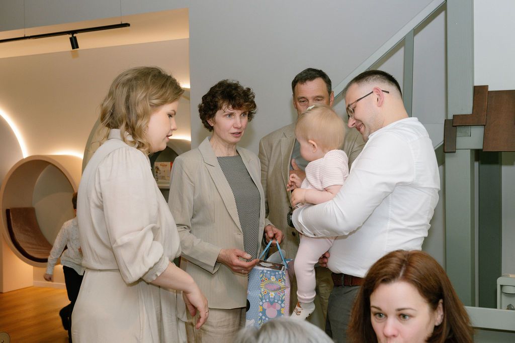 Adults and a baby gather in a modern interior space, engaged in conversation near a staircase.