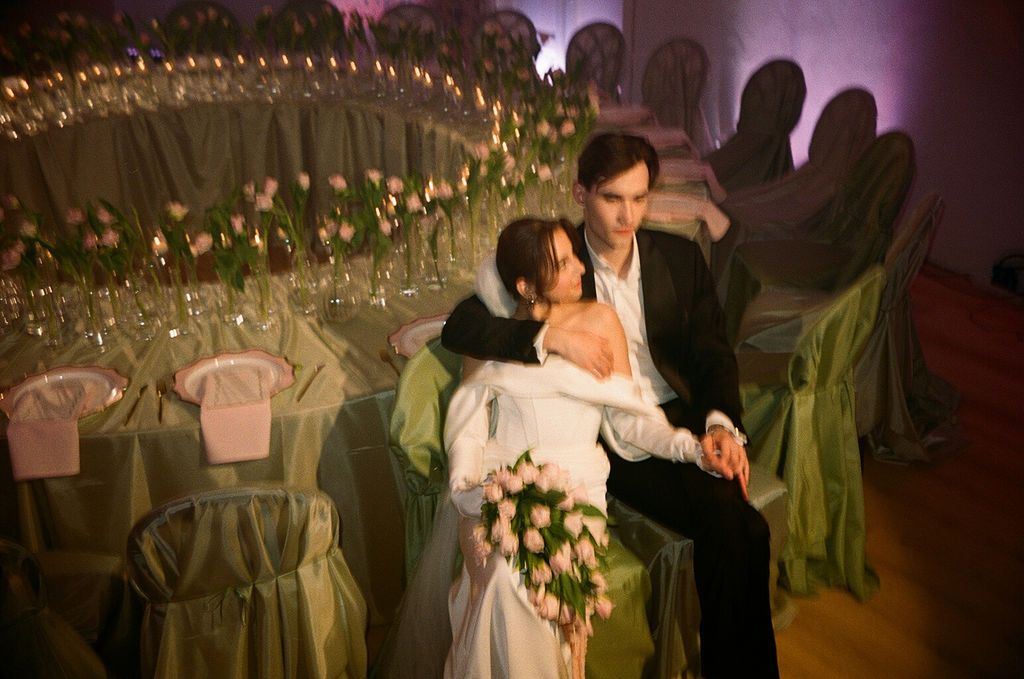 Bride and groom sitting together at elegantly decorated wedding reception with green chair covers and floral centerpieces.