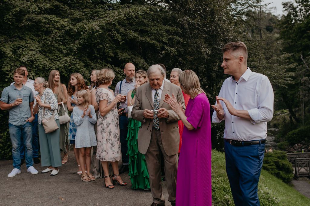 Guests gathered outdoors at a wedding reception, socializing on a garden path surrounded by lush greenery.