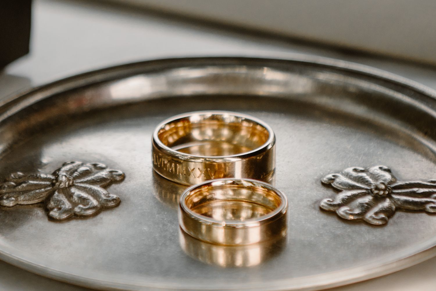 Two gold wedding rings displayed on a decorative silver tray with floral embellishments.
