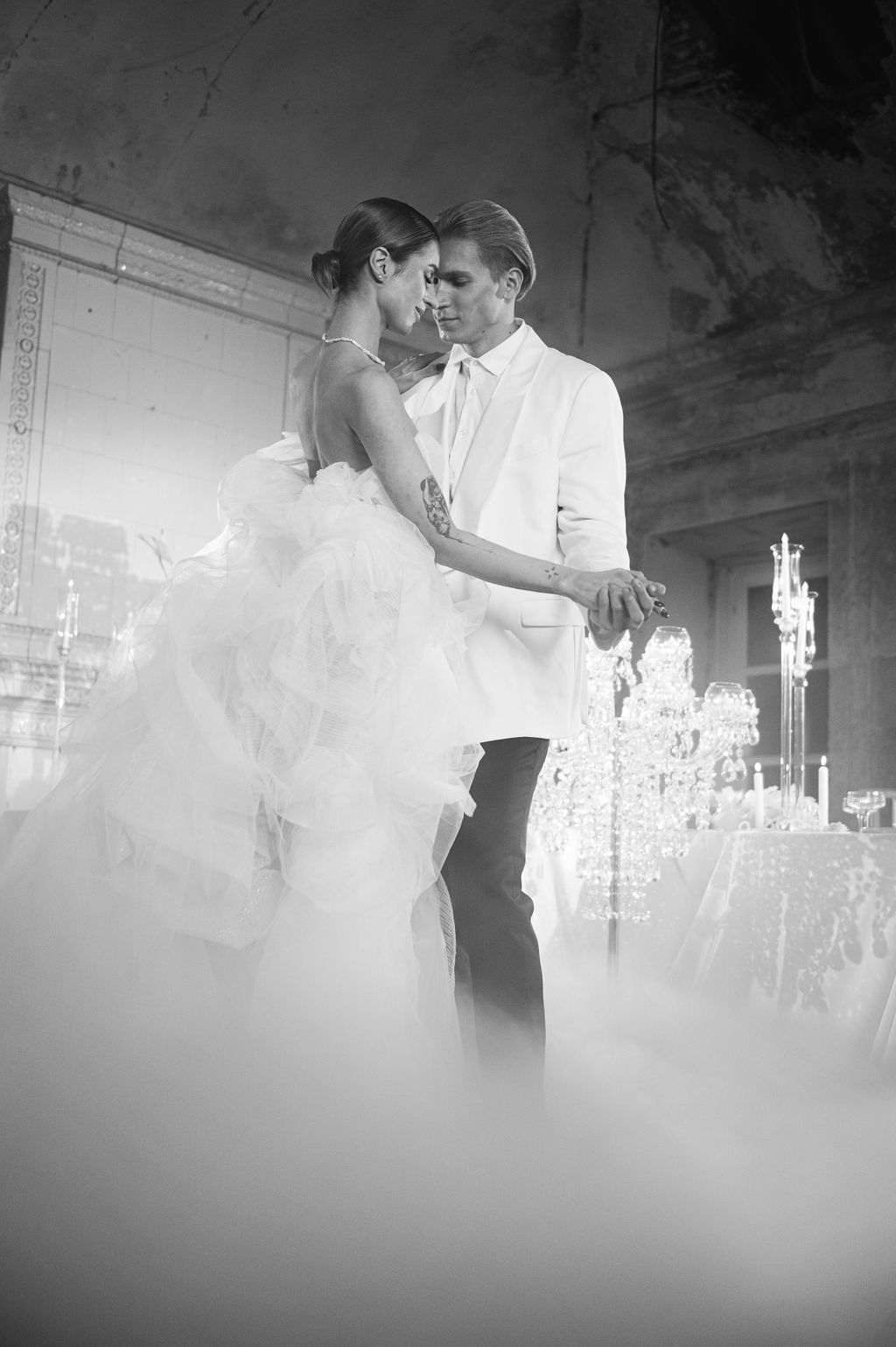 Black and white photo of a bride and groom sharing their first dance surrounded by elegant chandeliers and misty fog.