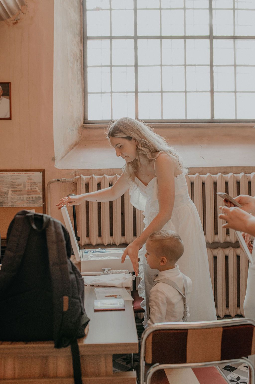 Bride in white dress helping young boy sign documents at a registry office desk.